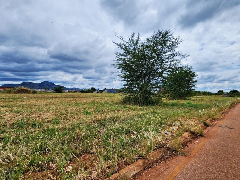 A vacant commercial land plot featuring direct paved road access and concrete curbing, situated in an open landscape setting.