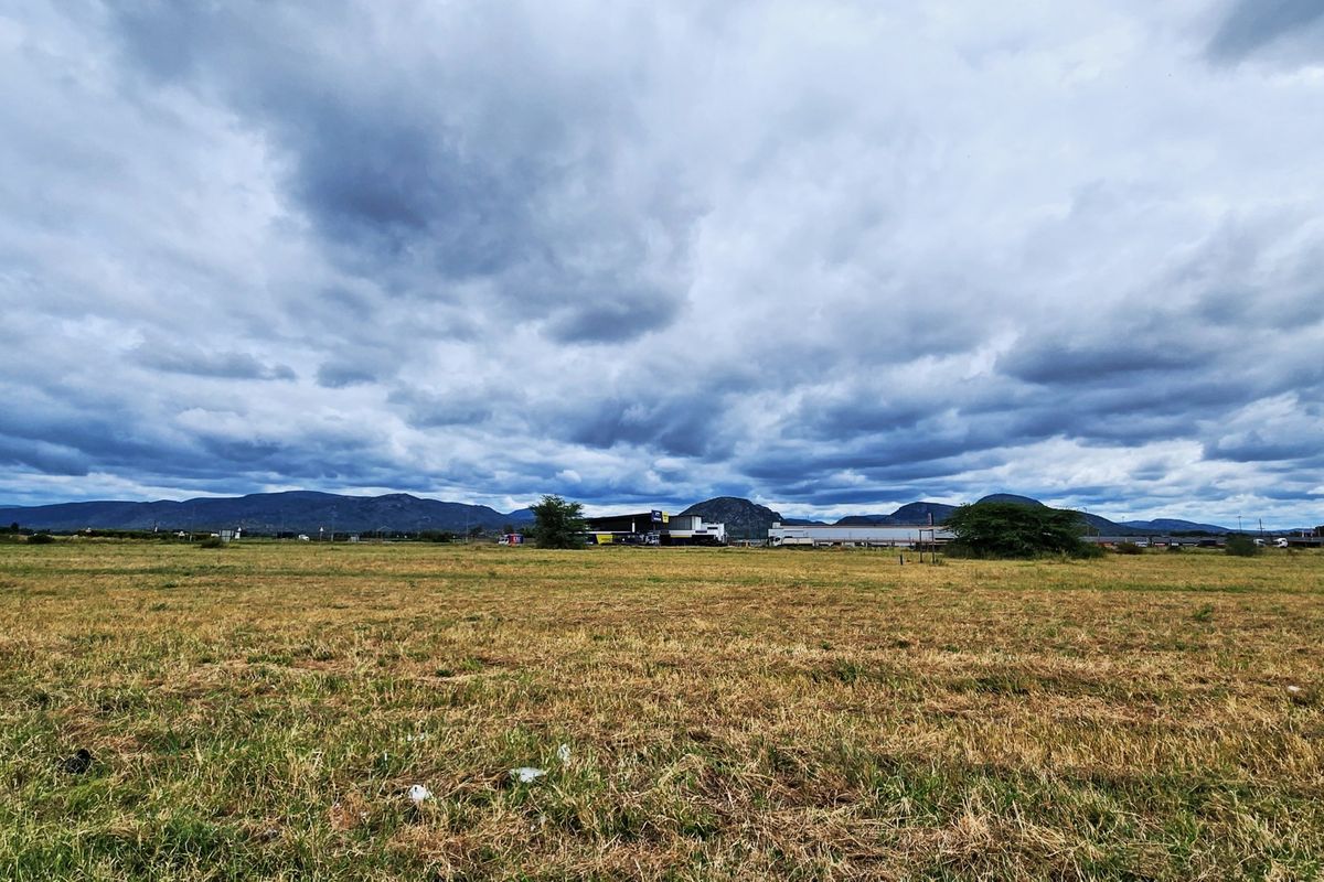 A wide-angle view of an expansive vacant commercial land plot featuring natural grass terrain and a scenic mountain range in the background.
