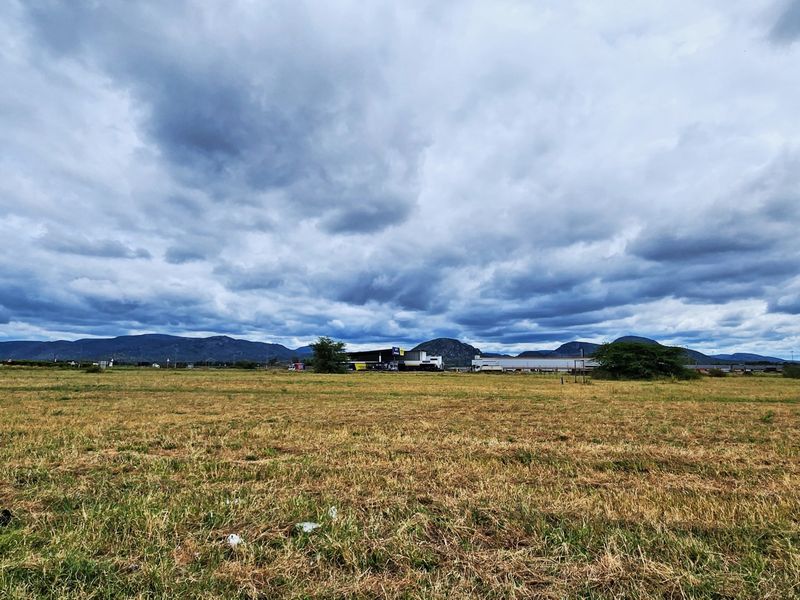 A wide-angle view of an expansive vacant commercial land plot featuring natural grass terrain and a scenic mountain range in the background.