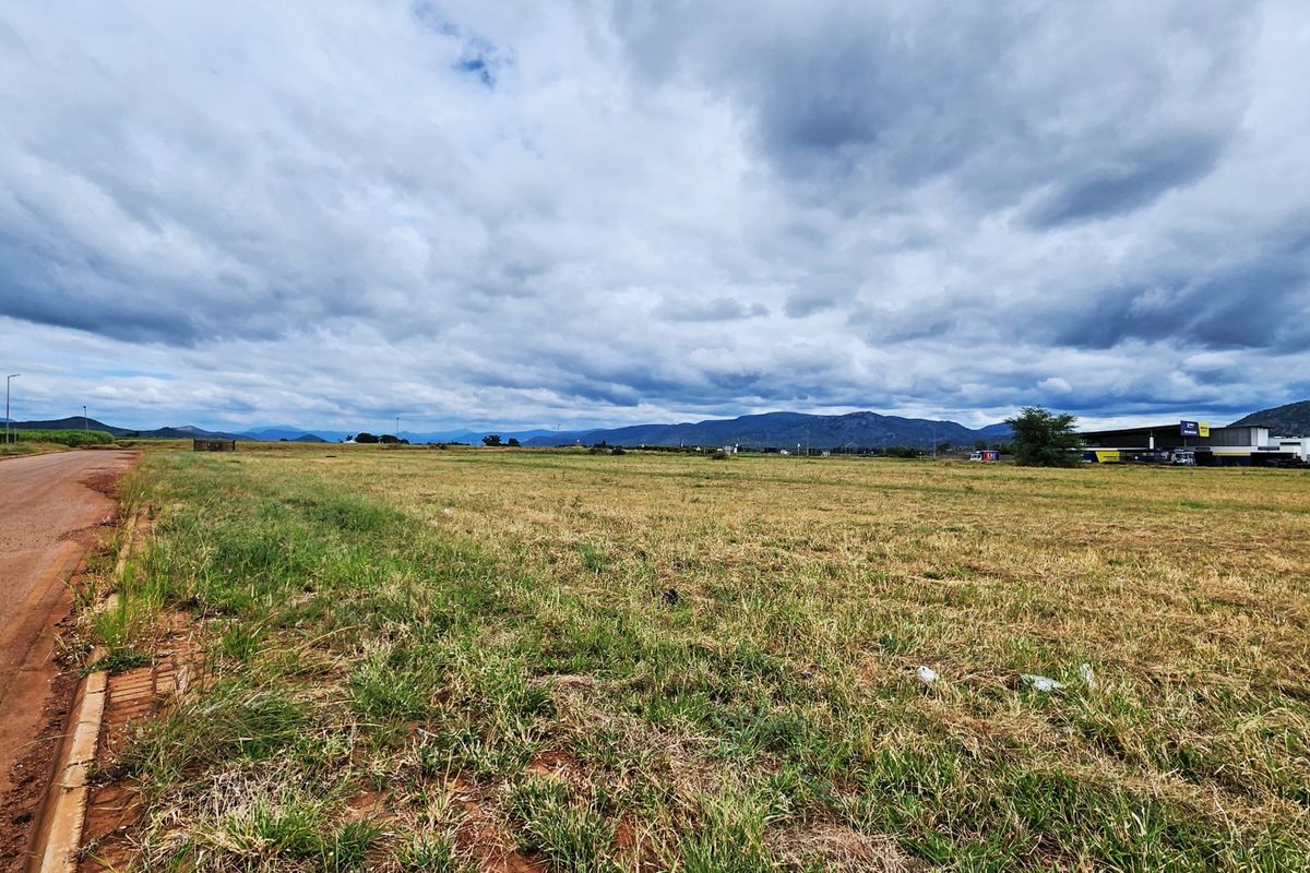 A wide-angle view of a vacant commercial land plot featuring direct road access and scenic mountain views in the distance.