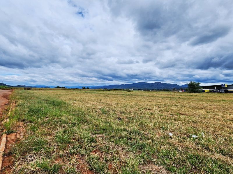 A wide-angle view of a vacant commercial land plot featuring direct road access and scenic mountain views in the distance.