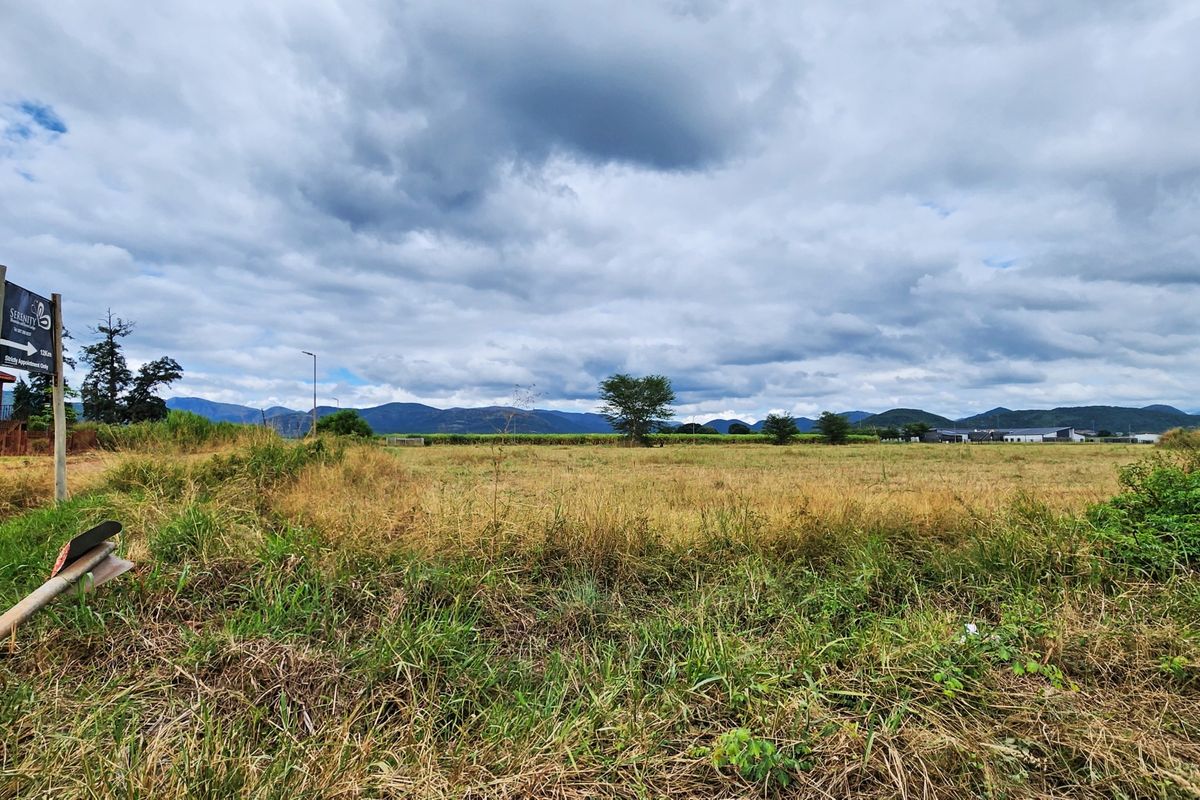 A wide-angle view of a vacant commercial land plot featuring natural grassland, perimeter fencing, and distant mountain views.