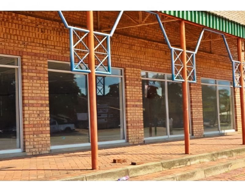 Front exterior view of a retail property featuring a brick facade, large glass display windows, and a covered paved walkway with metal support columns.