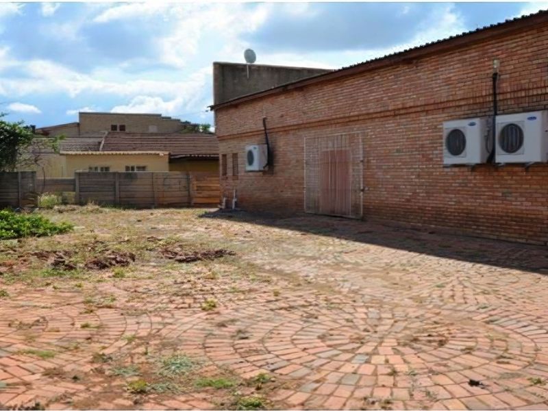 Rear exterior area featuring brick paving, perimeter fencing, and wall-mounted air conditioning units, offering potential for outdoor space improvement.