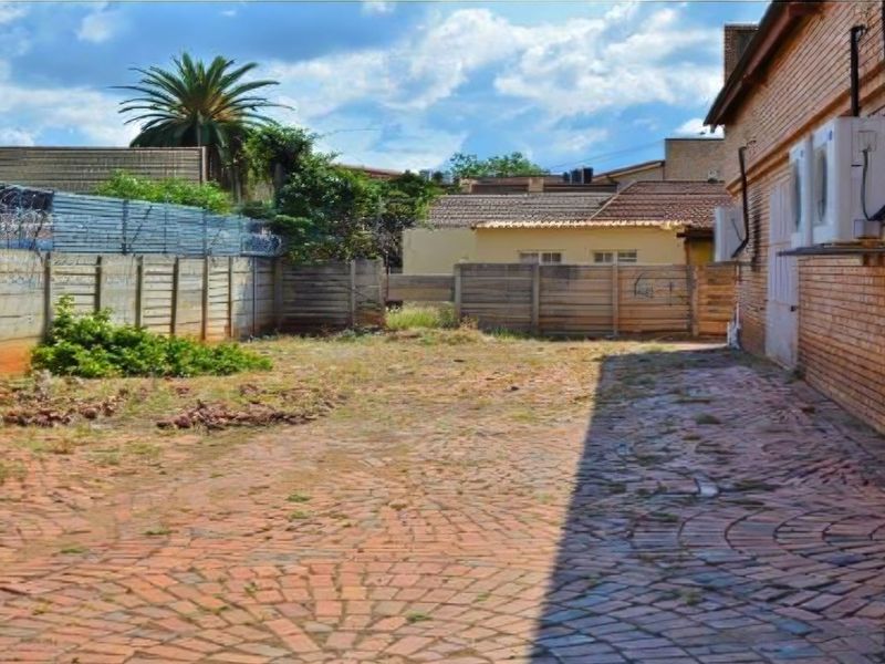 Rear exterior area featuring brick paving, perimeter fencing with security wire, and wall-mounted air conditioning units.