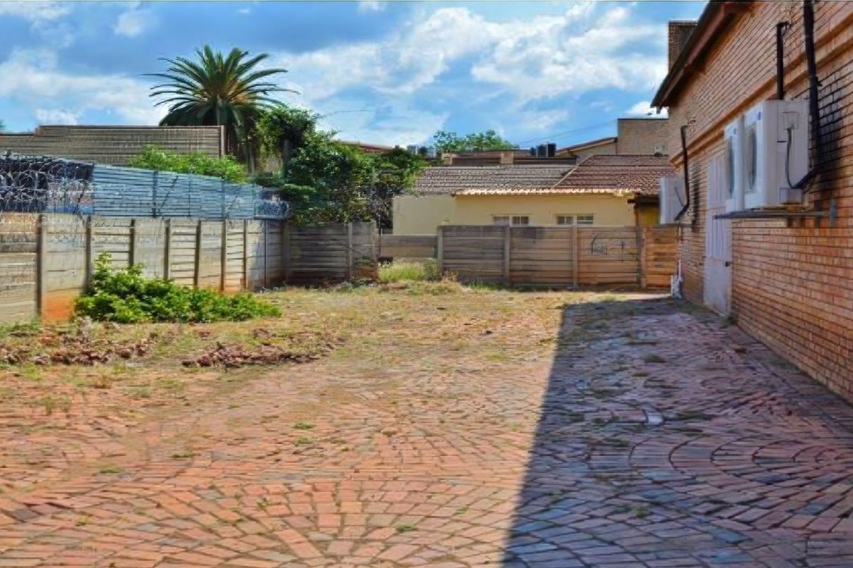 Rear exterior area featuring brick paving, perimeter fencing with security wire, and wall-mounted air conditioning units.