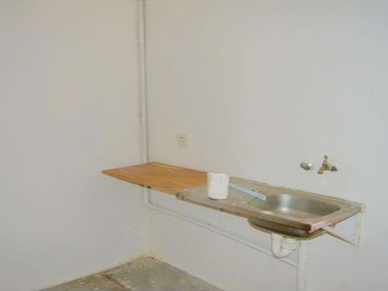 A basic utility or laundry area featuring a simple stainless steel sink, wall-mounted shelf, and exposed plumbing fixtures in a shell-condition space.