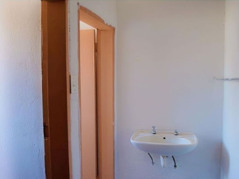 A basic, empty bathroom space featuring a wall-mounted basin and simple door frames, requiring cosmetic updates and finishing touches.