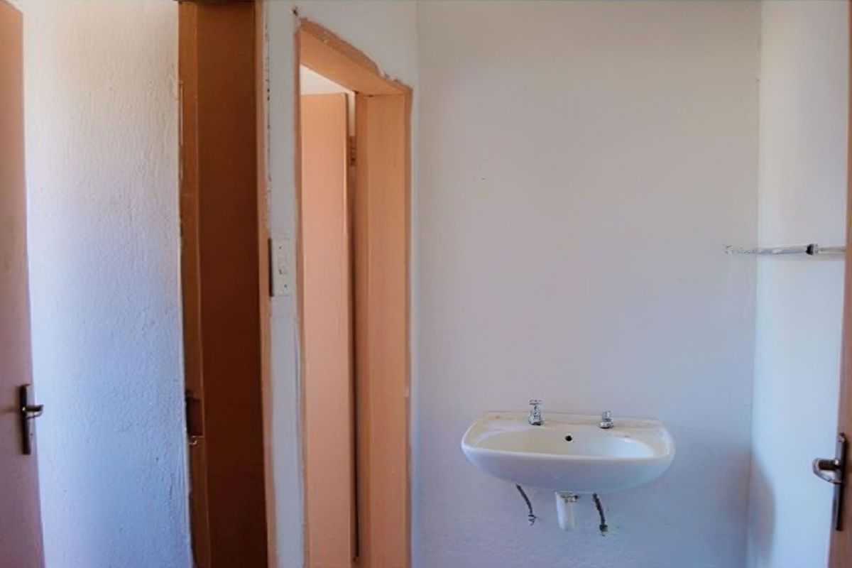 A basic, empty bathroom space featuring a wall-mounted basin and simple door frames, requiring cosmetic updates and finishing touches.