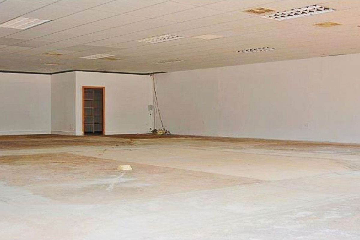A large, vacant open-plan retail space featuring a suspended ceiling, recessed lighting, and unfinished flooring, requiring significant refurbishment.