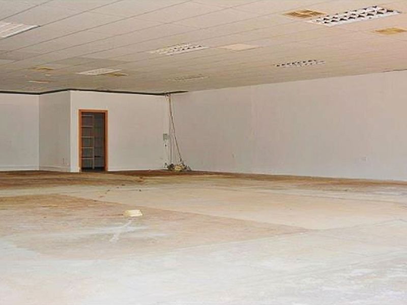 A large, vacant open-plan retail space featuring a suspended ceiling, recessed lighting, and unfinished flooring, requiring significant refurbishment.
