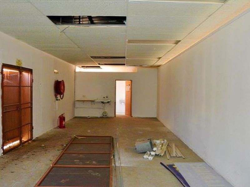 An empty utility or storage space featuring a drop ceiling with missing tiles, a wall-mounted sink, and a security gate entrance.