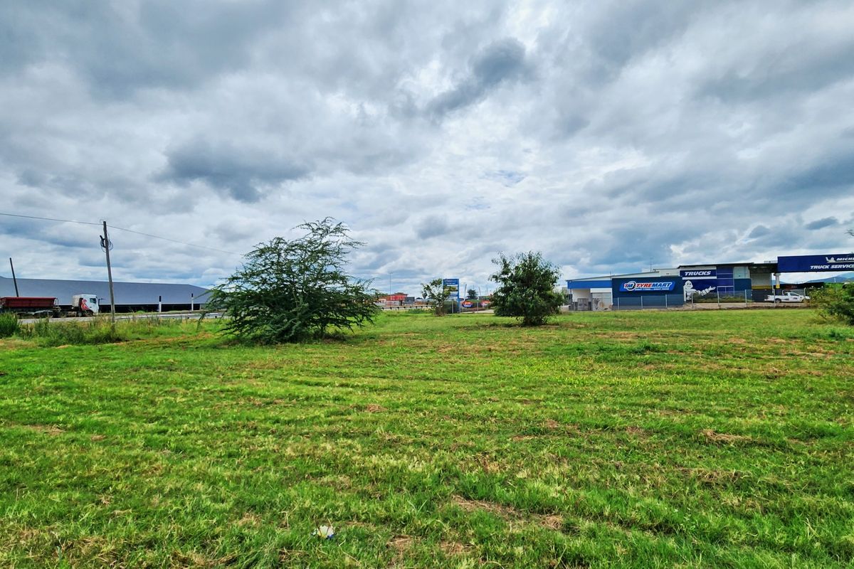 A wide-angle view of a vacant commercial land plot featuring open grass areas with surrounding commercial infrastructure and utility poles.