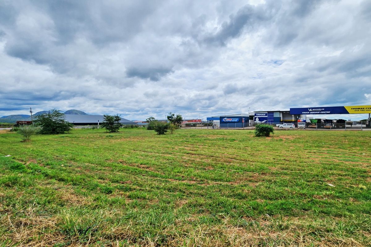 A view of a vacant commercial land plot with surrounding industrial buildings and a tyre service centre in the background.
