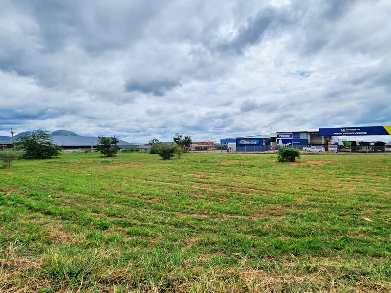 A view of a vacant commercial land plot with surrounding industrial buildings and a tyre service centre in the background.