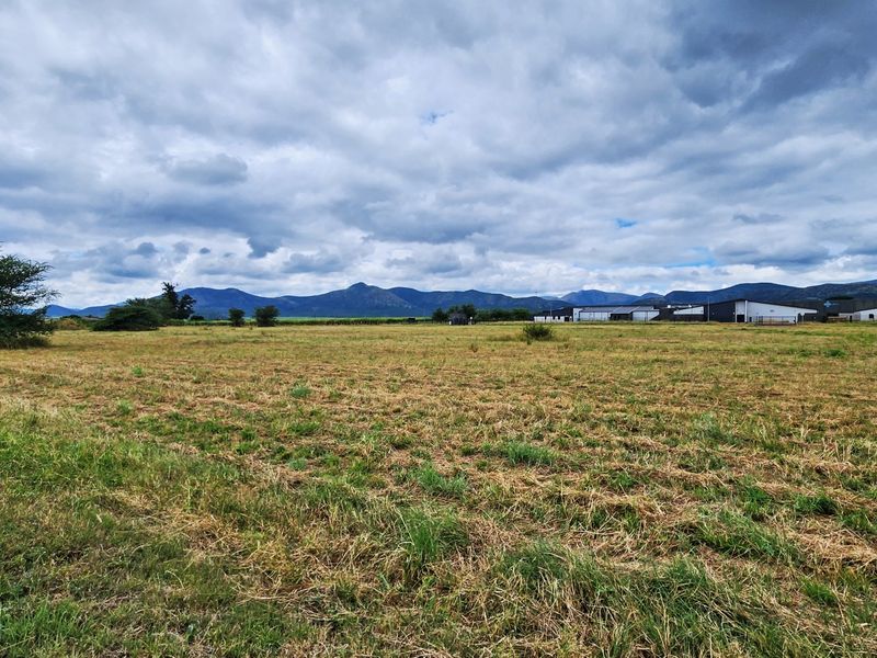A wide-angle view of the vacant commercial land featuring expansive open fields with a scenic mountain range backdrop.