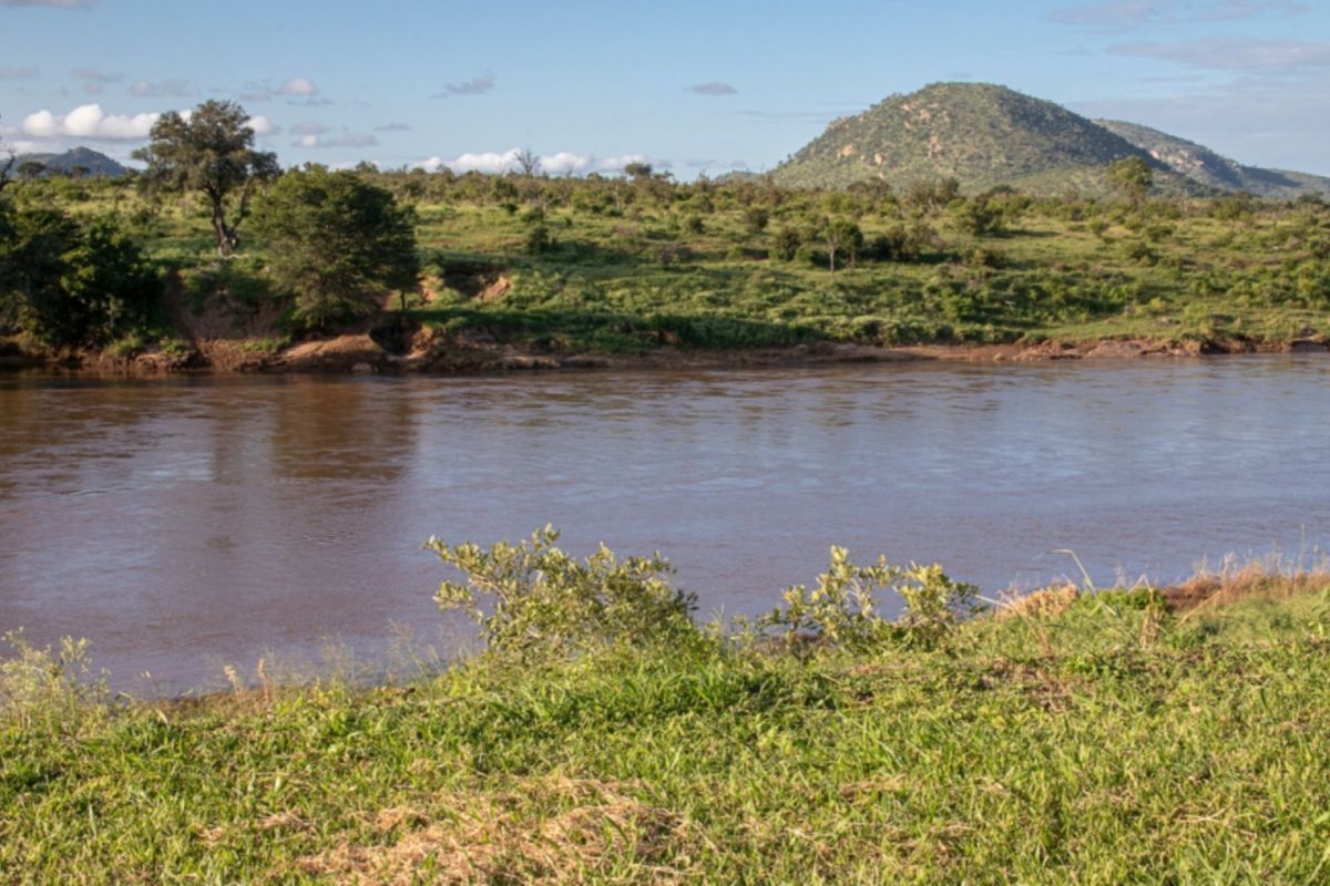 A scenic view of a natural river flowing through a landscape with lush vegetation and distant hills.