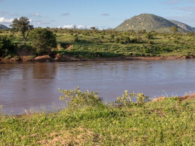 A scenic view of a natural river flowing through a landscape with lush vegetation and distant hills.