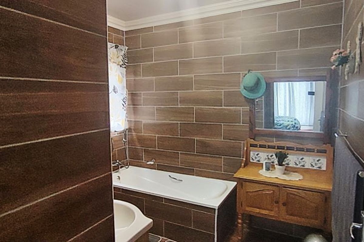 A bathroom featuring wood-look wall tiling, a built-in bathtub, and a vanity unit with a mirror.