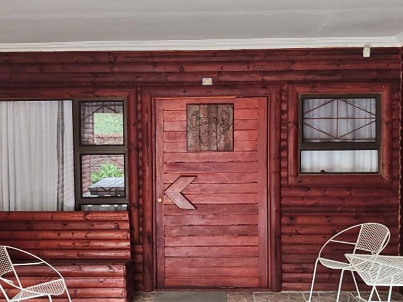 Covered patio area featuring rustic log cabin style timber wall cladding, a solid timber entrance door, and built-in bench seating.