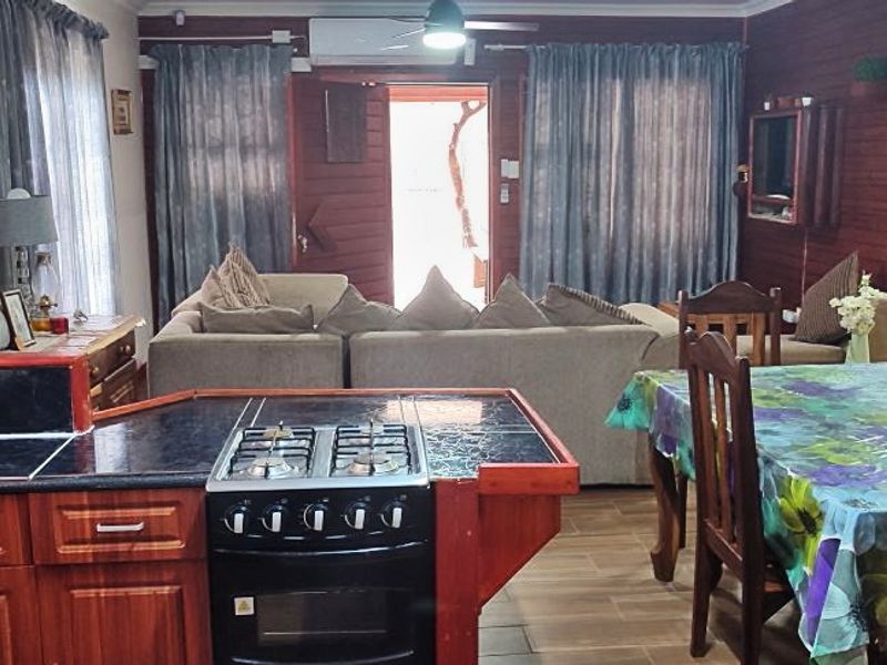 Open plan living and kitchen area featuring timber wall paneling, tiled flooring, and a functional kitchen layout with built-in cabinetry and gas cooking appliances.