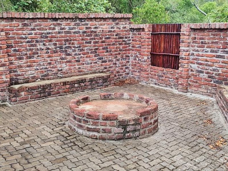 Outdoor entertainment area featuring a central brick fire pit, built-in brick seating, and paved flooring enclosed by rustic brick boundary walls.