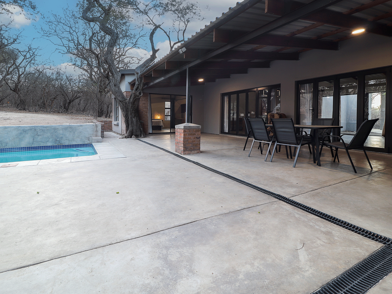 A spacious covered concrete patio featuring a built-in drainage system, overlooking a swimming pool with direct access to the interior through sliding glass doors.