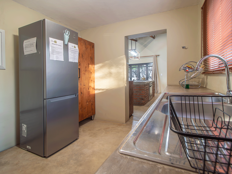 A functional scullery area featuring a stainless steel double sink, concrete flooring, and venetian blinds, with a view through to the adjacent living space.