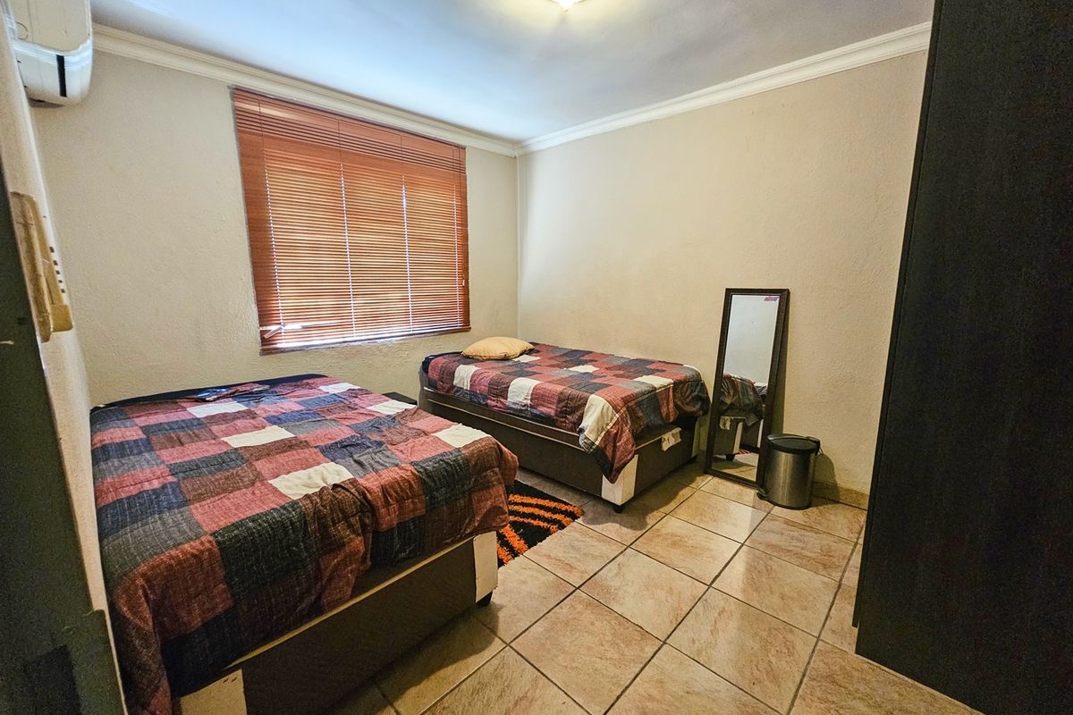 A bedroom featuring tiled flooring, a window with fitted blinds, and a wall-mounted air conditioning unit.