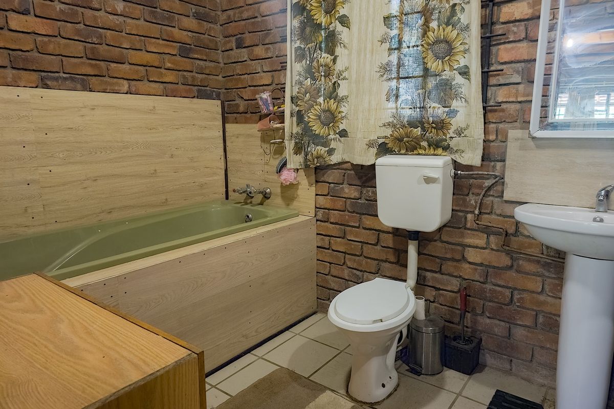 A rustic-style bathroom featuring exposed brick walls, a green bathtub with light wood-look paneling, a pedestal sink, and a standard toilet.