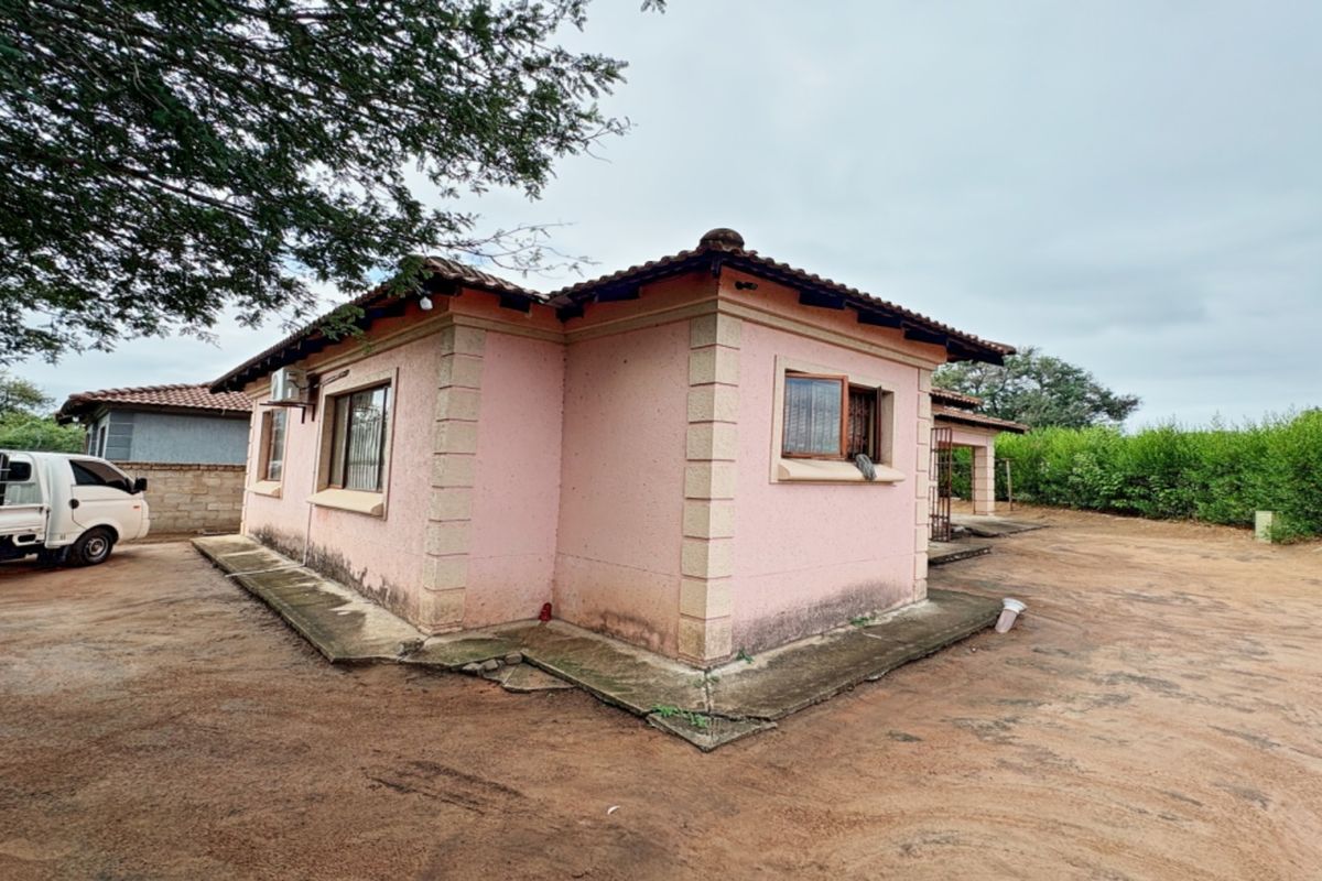 Rear view of a single-story house featuring a tiled roof, concrete apron, and security bars on the windows.