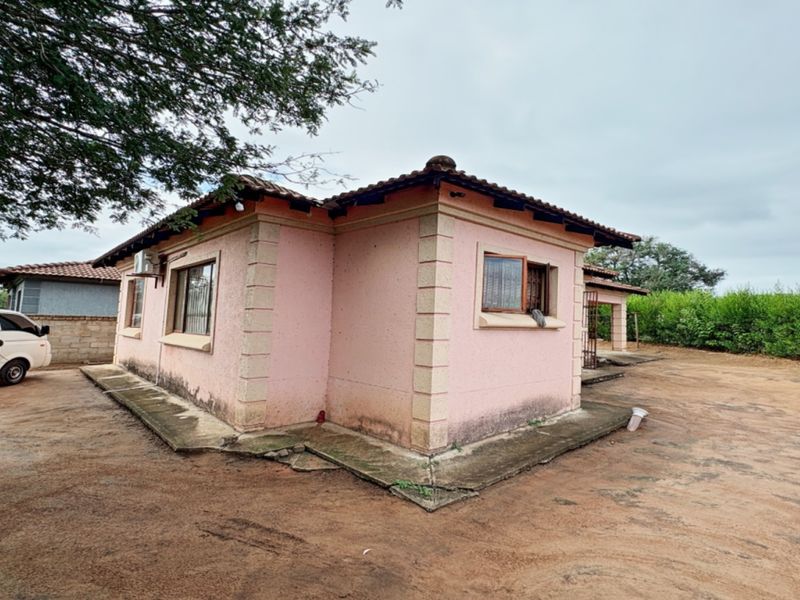 Rear view of a single-story house featuring a tiled roof, concrete apron, and security bars on the windows.