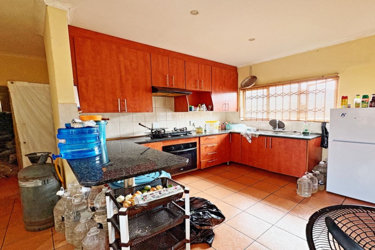 A functional kitchen featuring wooden cabinetry, granite countertops, a built-in oven, gas hob, and tiled flooring, offering a practical layout for daily meal preparation.