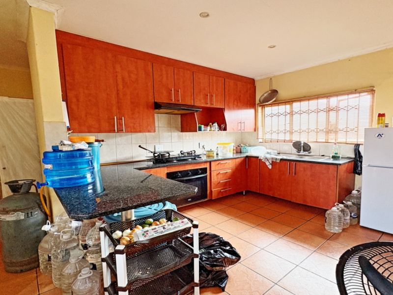 A functional kitchen featuring wooden cabinetry, granite countertops, a built-in oven, gas hob, and tiled flooring, offering a practical layout for daily meal preparation.