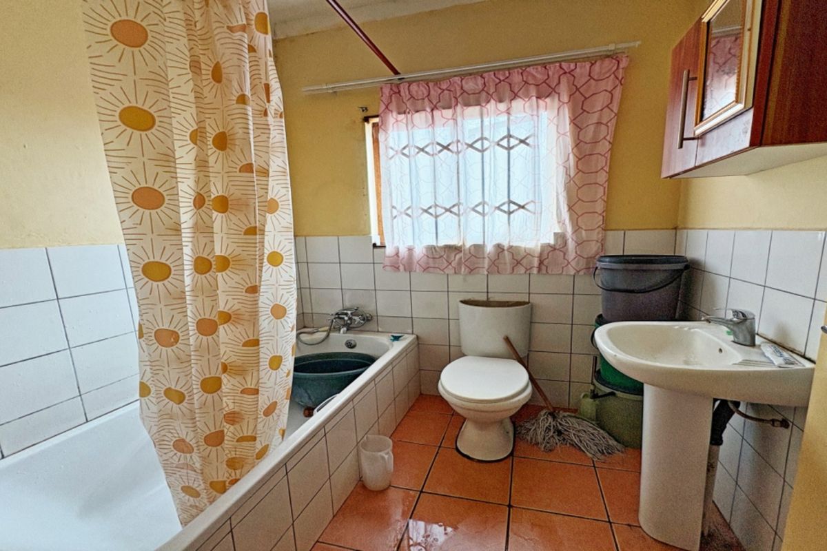 A functional bathroom featuring a bathtub, pedestal basin, and toilet with tiled walls and flooring, offering potential for modernization and cosmetic updates.