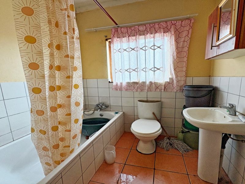 A functional bathroom featuring a bathtub, pedestal basin, and toilet with tiled walls and flooring, offering potential for modernization and cosmetic updates.