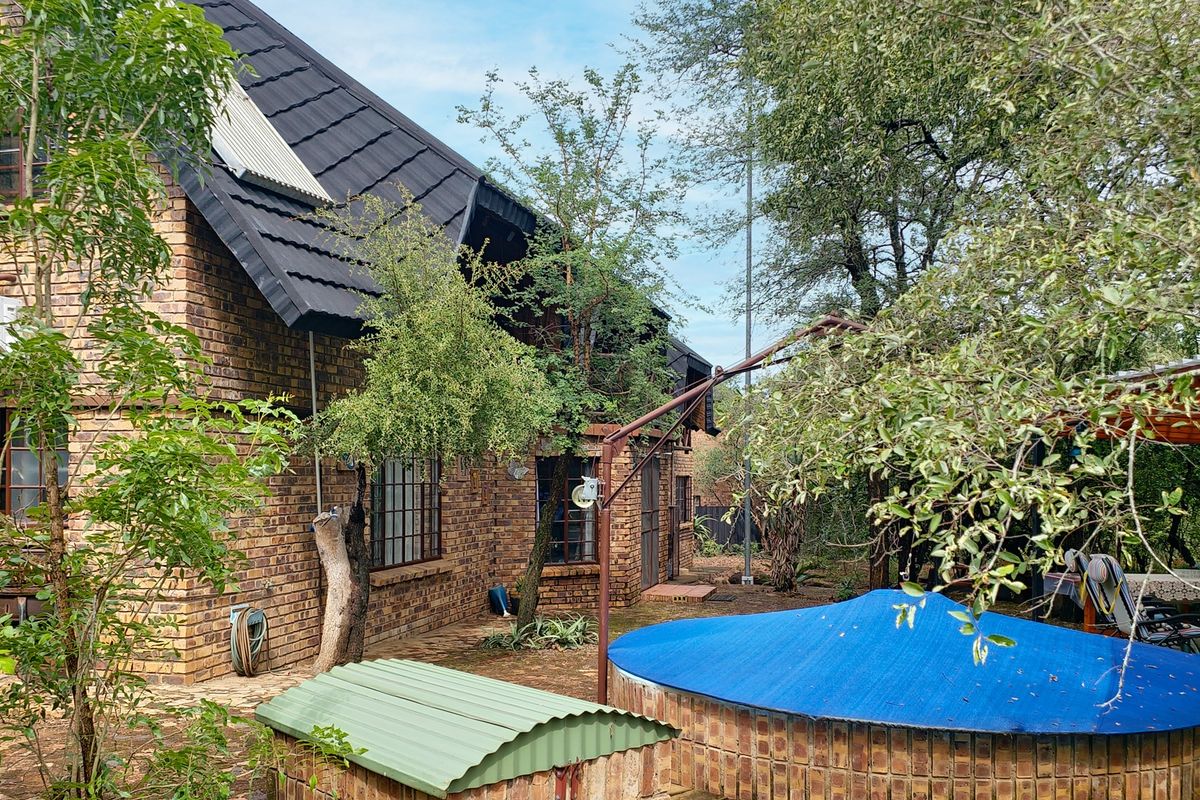 Rear view of a face brick house featuring a swimming pool with a cover and established garden surroundings.