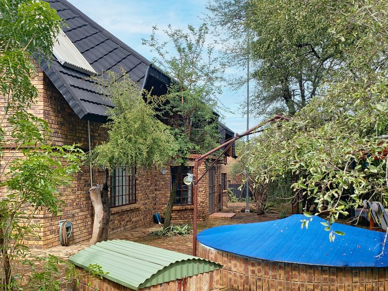 Rear view of a face brick house featuring a swimming pool with a cover and established garden surroundings.