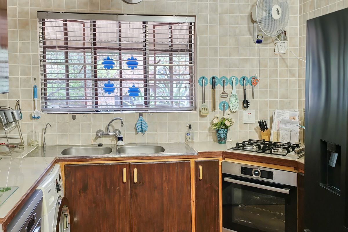 A functional kitchen featuring wooden cabinetry, a double basin stainless steel sink, a built-in oven, and a gas hob with tiled wall finishes.