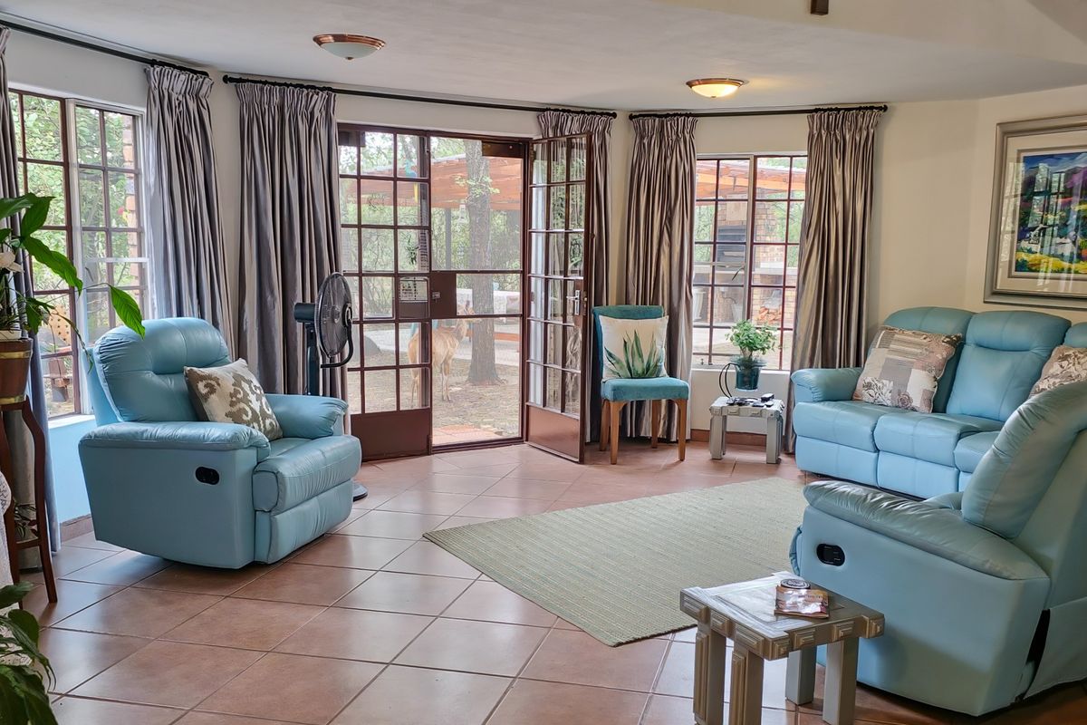 A bright living room featuring tiled flooring, large windows, and double french doors providing direct access to the outdoor garden area.