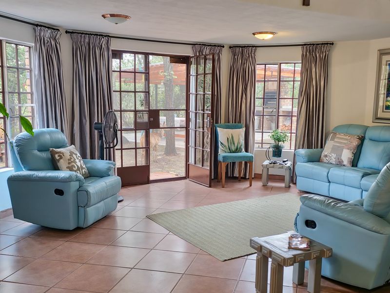 A bright living room featuring tiled flooring, large windows, and double french doors providing direct access to the outdoor garden area.