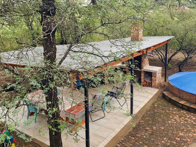 Covered outdoor patio featuring a built-in brick braai, tiled flooring, and adjacent brick-clad plunge pool set within a natural garden environment.