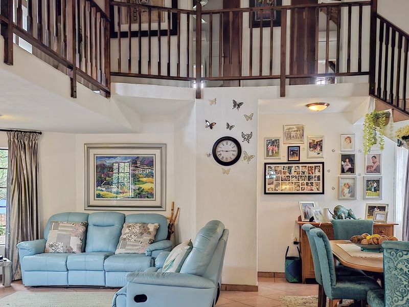 Open plan living and dining area featuring a double volume ceiling, wooden staircase with balustrade, and a mezzanine level overlooking the main living space.