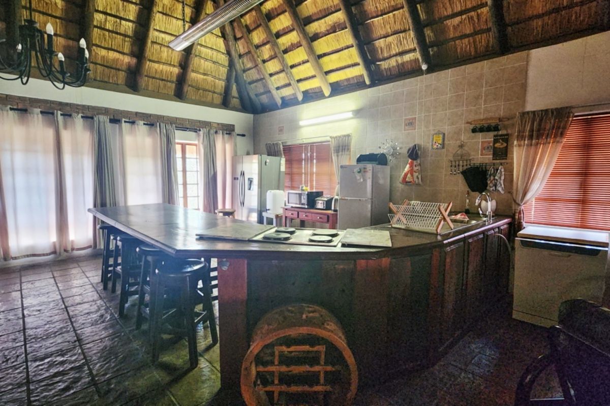 Spacious kitchen featuring a unique high thatched ceiling with exposed rafters, a large breakfast bar, and tiled flooring throughout.