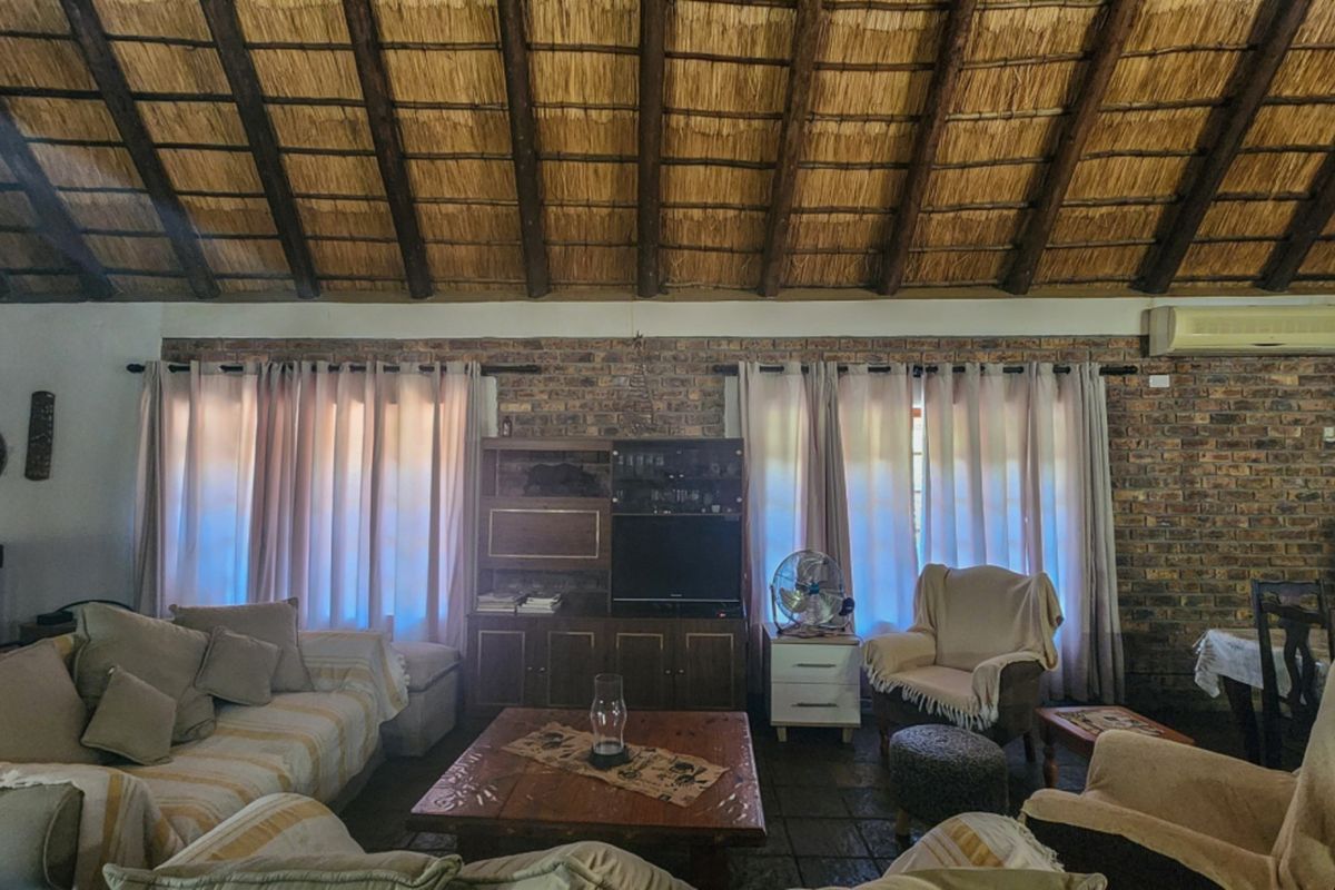 Spacious living area featuring a high exposed thatch ceiling, rustic exposed brick walls, and tiled flooring, creating a warm and traditional atmosphere.