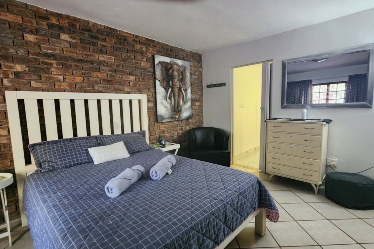 A bedroom featuring an exposed brick accent wall, tiled flooring, and direct access to a walk-in closet area with built-in storage.