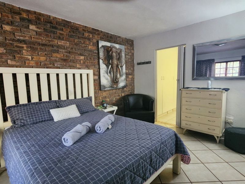 A bedroom featuring an exposed brick accent wall, tiled flooring, and direct access to a walk-in closet area with built-in storage.