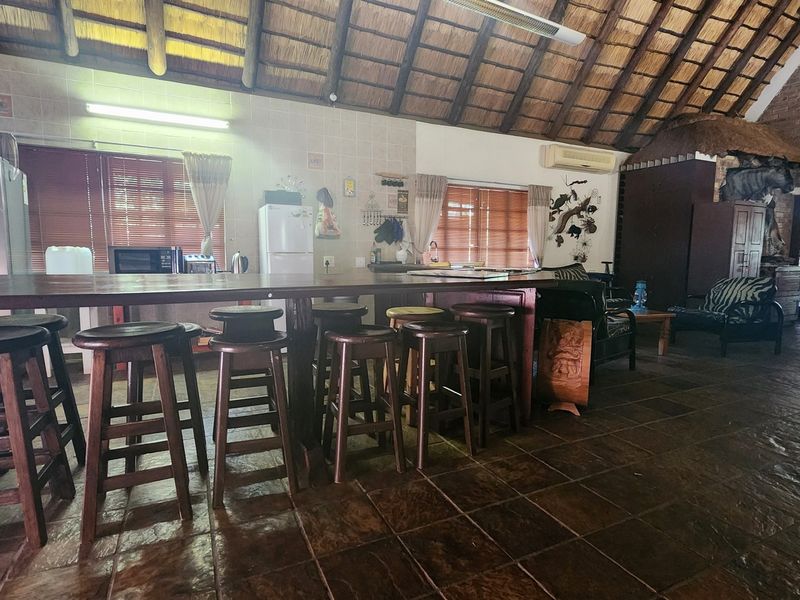 Spacious open-plan living area featuring a high thatched roof with exposed timber rafters, stone tile flooring, and a large built-in breakfast bar.