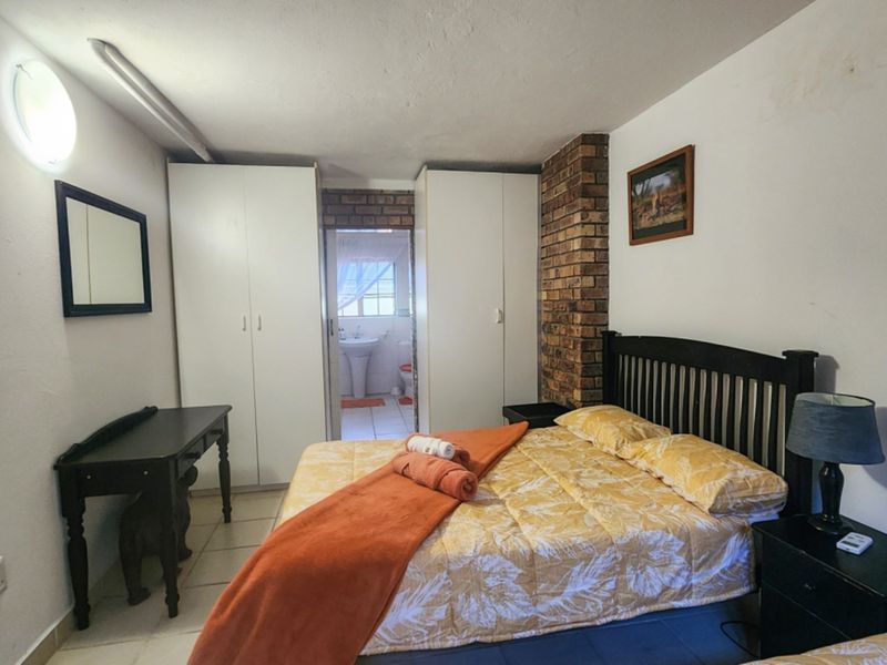 Bedroom featuring built-in cupboards, an exposed brick accent wall, and tiled flooring, with an adjoining bathroom visible through the doorway.