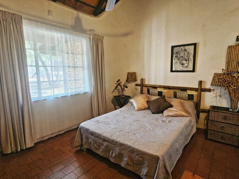 A rustic bedroom featuring exposed timber ceiling beams, a thatched roof, and terracotta floor tiles, offering a cozy, traditional atmosphere.